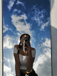 a woman taking a selfie with her cell phone in front of the sky and clouds