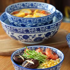 three blue and white bowls filled with food on top of a wooden table next to another bowl