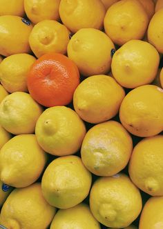 a bowl full of lemons with an orange in the middle