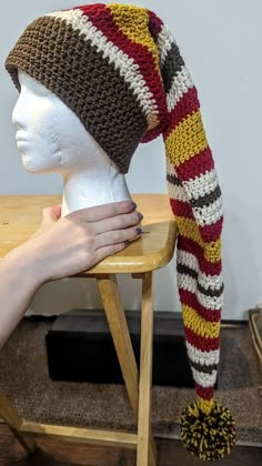 a crocheted hat on top of a wooden chair next to a mannequin's head