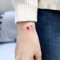 a woman's hand with a small red dot tattoo on it