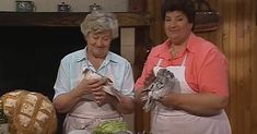 two women in aprons standing next to each other holding bread and looking at something