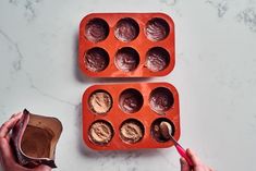 two people are decorating chocolates in muffin tins on a marble table