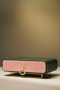 a green and pink case with a gold ring on the front sitting on a table