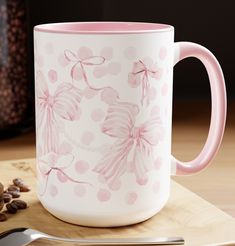 a pink and white coffee mug sitting on top of a wooden cutting board next to a spoon