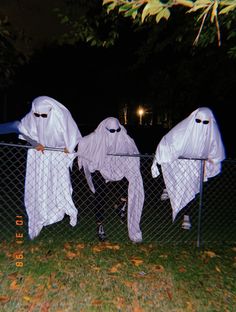 three white ghost costumes hanging on a fence in the dark, with one person standing next to them