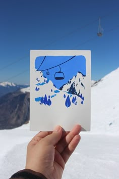 a hand holding up a piece of paper with a ski lift in the sky above it