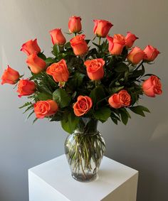 a vase filled with lots of orange roses on top of a white table next to a wall