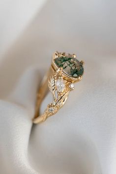 a gold ring with a green and white stone in it's center on a white cloth