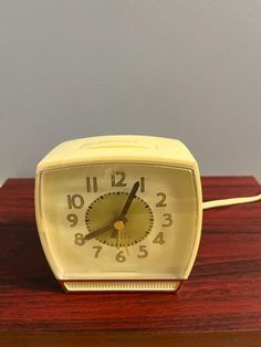 an alarm clock sitting on top of a wooden table next to a wall with a gray background