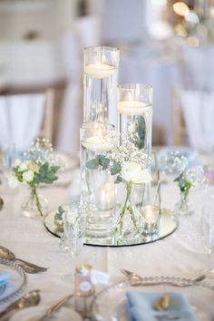 candles and flowers in glass vases on a white table cloth with silverware, plates and napkins