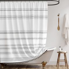 a white bath tub sitting next to a wooden floor covered in a black and white striped shower curtain