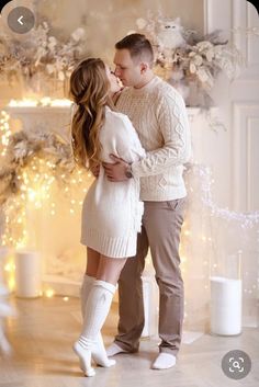 a man and woman standing next to each other in front of a fireplace with christmas lights