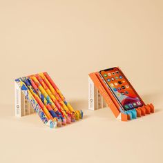 an orange and blue cell phone is next to a stack of colored pencils