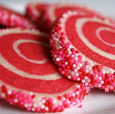 some red and white cookies with sprinkles on them sitting on a plate