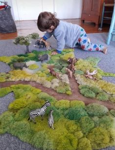 a little boy playing with toy animals on the floor in front of a play area