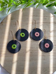 three circular earrings with green and pink beads on a wooden table next to leaves in the sun