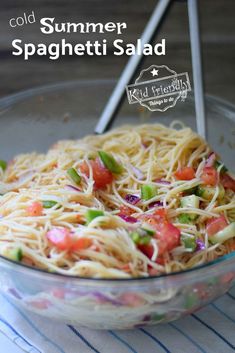 a glass bowl filled with spaghetti salad on top of a table