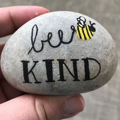 a hand holding a rock with the words bee kind painted on it and a honeybee