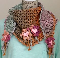 a crocheted scarf with flowers and hearts hanging from it's sides on a mannequin head