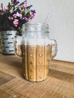 a glass jar filled with liquid sitting on top of a wooden table next to flowers