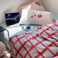 a laptop computer sitting on top of a bed next to two pillows and a blanket