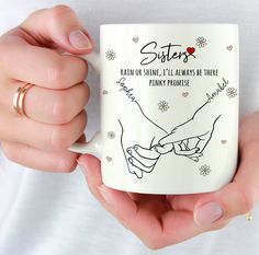 two hands holding a coffee mug that says sisters and each other's names on it