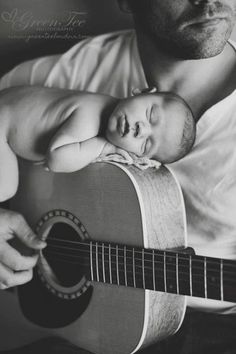 a black and white photo of a man holding a guitar with a baby sleeping on it