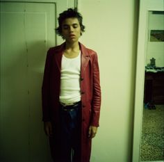 a man standing in front of a door wearing a long red coat and white t - shirt