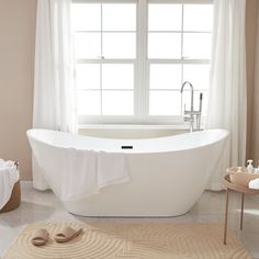 a white bath tub sitting under a window next to a rug on top of a floor