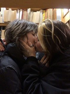 two women kissing each other in front of bookshelves