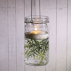 a mason jar filled with moss and lit candles hanging from a chain on a white wooden wall