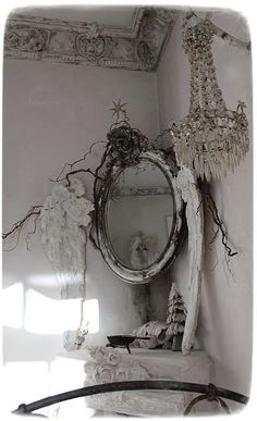 an old mirror is hanging on the wall next to a shelf with flowers and branches