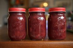 three jars filled with red liquid sitting on top of a wooden table