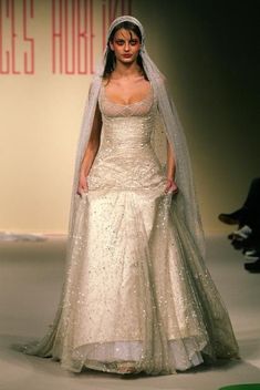 a woman is walking down the runway wearing a wedding dress and veil with sequins on it