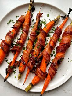 bacon wrapped carrots on a white plate with parsley sprinkled around them