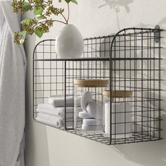 a wire shelf with towels and toiletries on it in front of a white wall