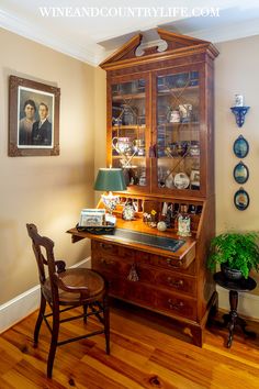 an old fashioned desk and chair in the corner of a room with pictures on the wall