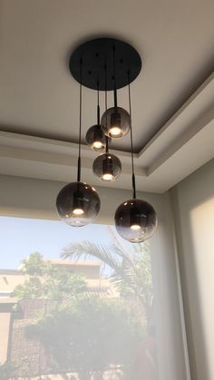 three lights hanging from the ceiling in front of a large window with palm trees outside