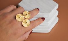 a woman's hand with three gold rings on top of her finger and two white napkins in the background