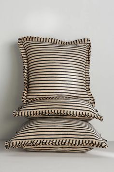 three pillows stacked on top of each other in front of a white wall with black and tan stripes