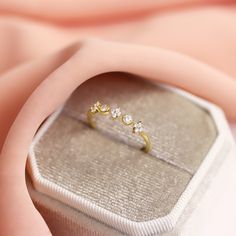 an open ring sitting on top of a white box next to a pink cloth covered surface