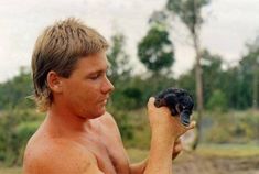 a shirtless man holding a bird in his right hand and looking at the ground