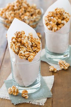 two glass cups filled with caramel popcorn on top of a wooden table