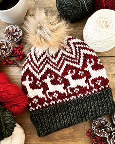 a red and white knitted hat next to balls of yarn, pineconis and a cup of coffee