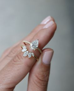 a woman's hand holding an engagement ring with three pear shaped diamonds on it