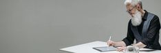 an older man sitting at a desk writing on a notepad