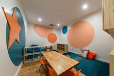 a room with blue and orange chairs, a wooden table and an art work on the wall