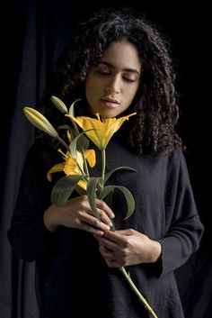 a woman holding a yellow flower in her hands