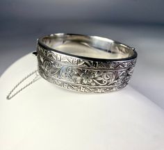 "Sterling Silver Bangle Bracelet with fine engraving. The design is boarded top and bottom of engraving in a triangular geometric  pattern. The interior panel is a floral motif. There is a dent in the panel but it doesn't take away from this beautiful piece with  history. The box closure works well and there is a safety chain.  Size: 3/4\" Width, Interior diameter 2 3/8\"  Thank you visiting HATTIE MAUDE VINTAGE  and please reach out with any questions, we are here to help!" Luxury Vintage Engraved Bangle, Luxury Ornate Sterling Silver Bangle, Luxury Antique Sterling Silver Bangle Bracelet, Formal Cuff Bangle Bracelet With 17 Jewels, Elegant Engraved Bangle, Classic Hallmarked Cuff Bracelet, Classic Etched Gold Bracelet For Formal Occasions, Heirloom Style Jubilee Bracelet, Classic Formal Cuff Bracelet With Intricate Design